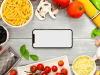 La imagen es una fotografía de plano general con vista superior (plano cenital) que muestra un smartphone con la pantalla en blanco en el centro, rodeado por una variedad de ingredientes.