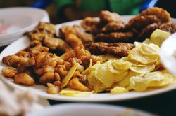 Uma porção variada de alimentos fritos, incluindo pedaços de frango e batatas fritas, dispostos em um prato grande. A apresentação destaca a venda de comida no delivery, com um foco em opções crocantes e apetitosas ideais para compartilhar ou consumir em ocasiões sociais.