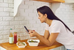 Mulher apoiada no balcão acompanhando a jornada do cliente pelo celular.
