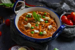 Prato de comida indiana com curry de paneer e legumes, servido em uma tigela azul.